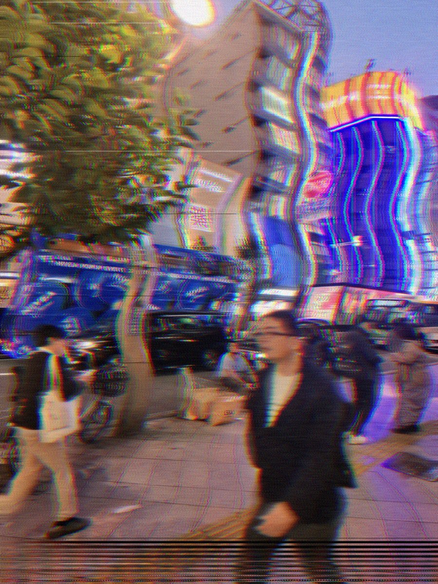 La même rue en VHS : la couleur qui bave latéralement depuis le néon, une déchirure de piste en bas de l'image, tout adouci comme une bande usée.