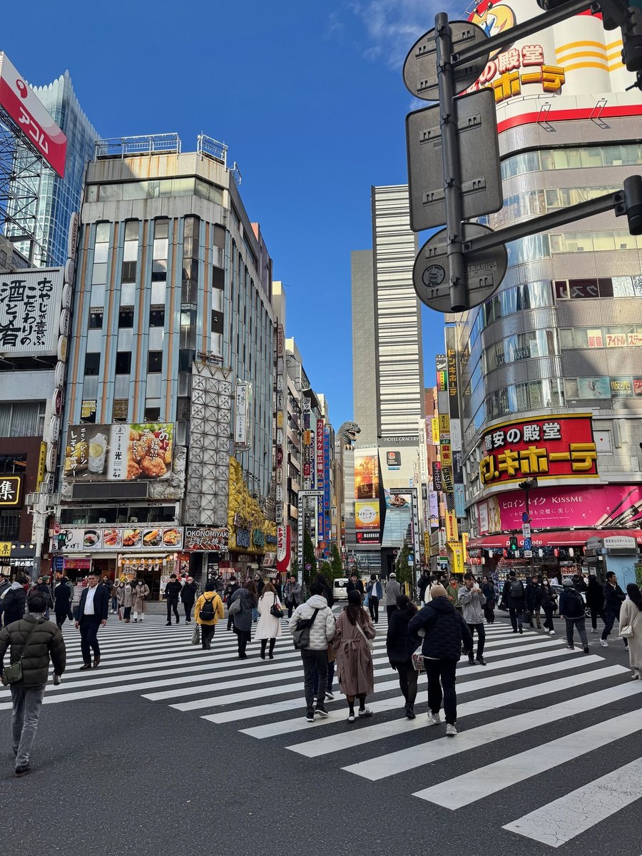 La photographie originale d'un carrefour de Tokyo par temps clair : tours de bureaux, enseignes, une foule sur le passage zébré.